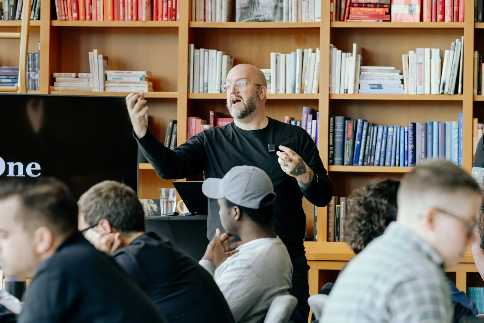 A speaker presenting to an engaged audience in front of the library wall