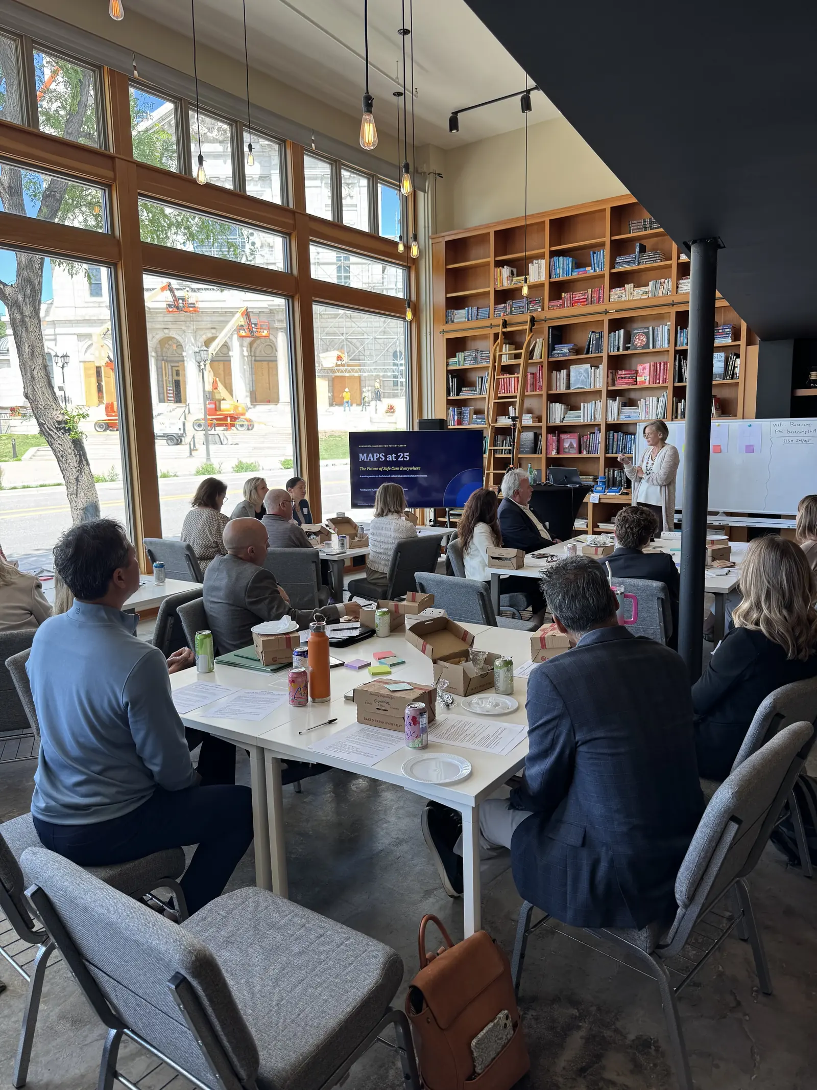 Workshop attendees at tables beside the windows, with a presentation on screen