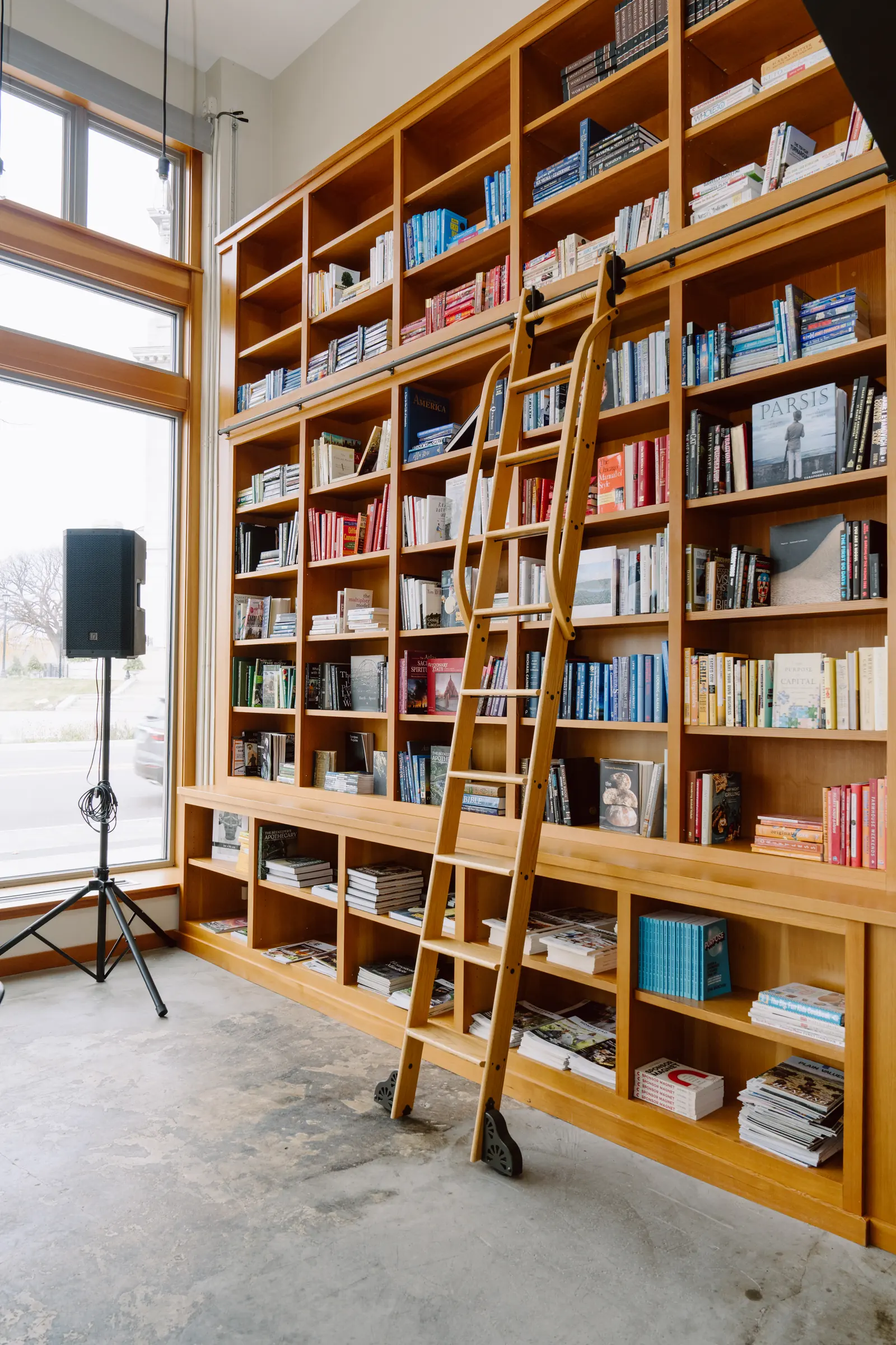 Library shelving and rolling ladder beside tall windows